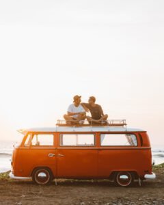 Zwei Freunde sitzen auf dem Dach ihres VW-Busses am Strand