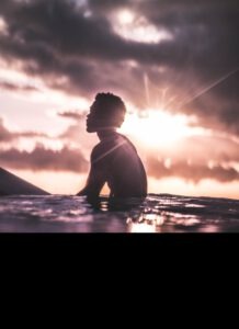Surfer sitzt vor Sonnenuntergang auf seinem Board